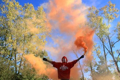 Rear view of person holding distress flare against trees