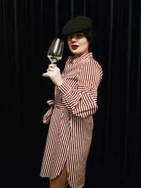 Portrait of woman having wine while standing against wall