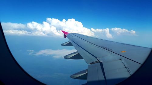 Cropped image of airplane flying in blue sky seen through window