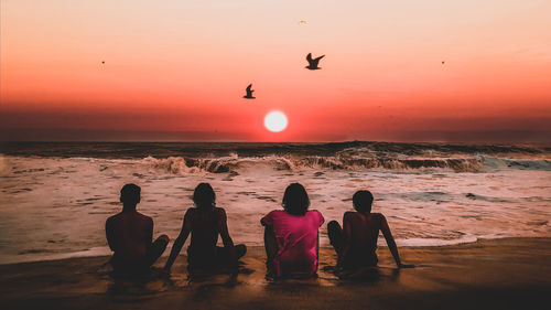 Rear view of people on beach during sunset