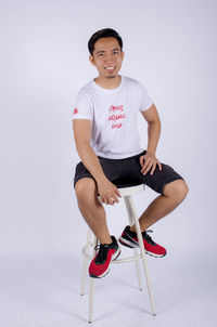 Portrait of young man sitting on seat against white background