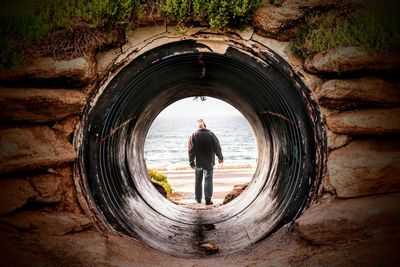 Rear view of man walking at beach seen through tunnel