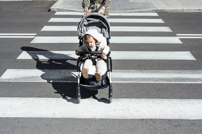 Mother with son in baby carriage crossing street in city on sunny day