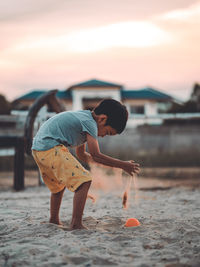 Boy playing on sand at beach during sunset