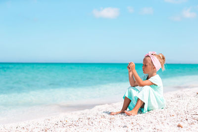 Rear view of woman sitting at beach against sky