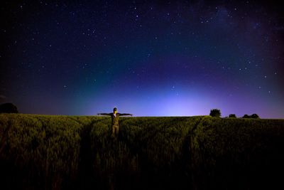 Man with arms outstretched standing on field against sky at night