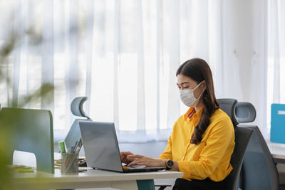 Woman wearing mask while sitting by laptop on table