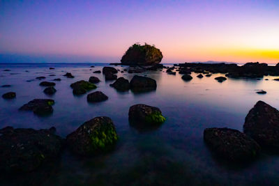 Rocks in sea against romantic sky at sunset