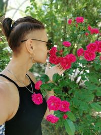 A brunette with a short haircut enjoys the smell of blooming roses in the park