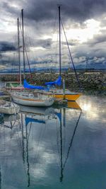 Boats in harbor against cloudy sky