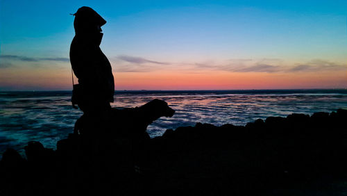 Silhouette woman standing at beach against sky during sunset