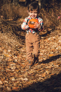 Portrait of boy holding pumpkin while walking on field