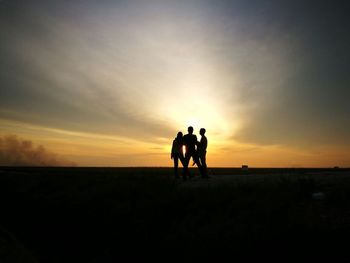 Silhouette men on landscape against sky during sunset