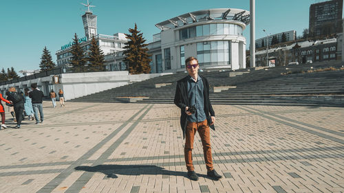 Man standing on footpath against buildings in city