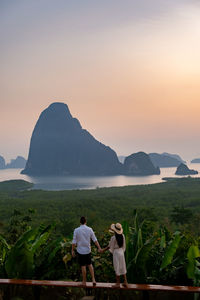 Rear view of men standing on mountain against sky during sunset