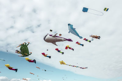 Low angle view of various colorful balloons flying against cloudy sky