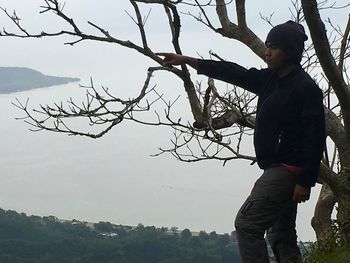 Man standing on bare tree against sky