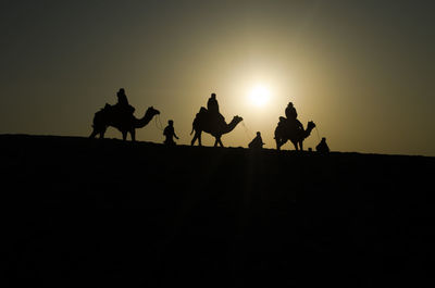 Silhouette people riding on desert against clear sky during sunset