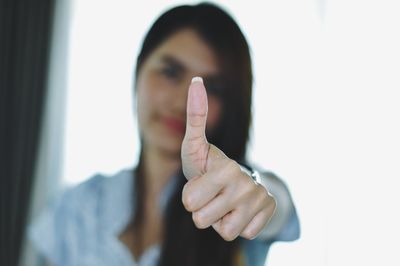 Portrait of mid adult woman showing thumbs up while standing against wall