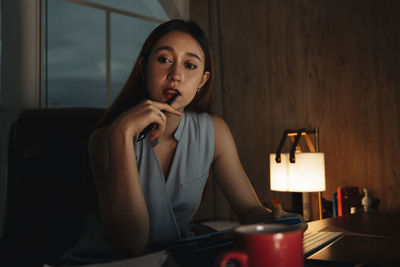 Cute girl holding pen brainstorming while sitting at home