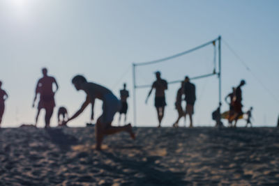 People playing soccer on beach against sky during sunset