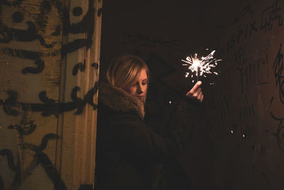 Woman holding illuminated sparkler in dark