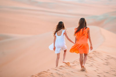 Rear view of women walking on sand at desert