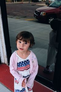 Portrait of cute girl standing by glass door