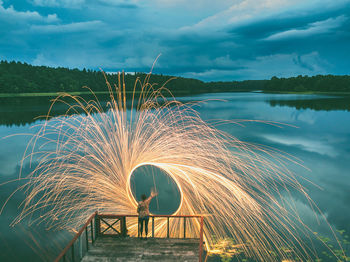 Woman with wire wool on jetty over lake against sky