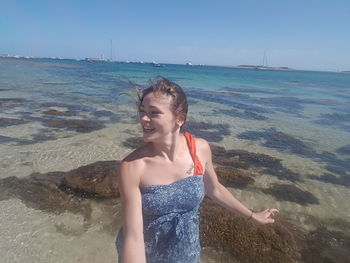 Beautiful young woman standing on beach against sky