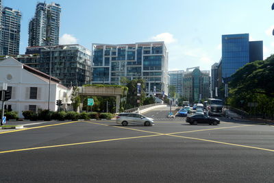 Cars on road by buildings against sky in city