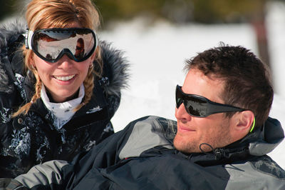 Portrait of smiling mid adult woman by man looking away on snowcapped mountain