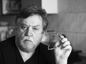 Close-up portrait of senior man holding eyeglasses at home