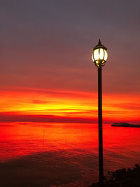 Street light by sea against orange sky