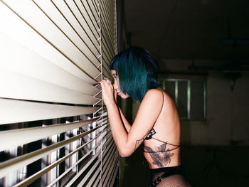 Side view of young woman looking through blinds