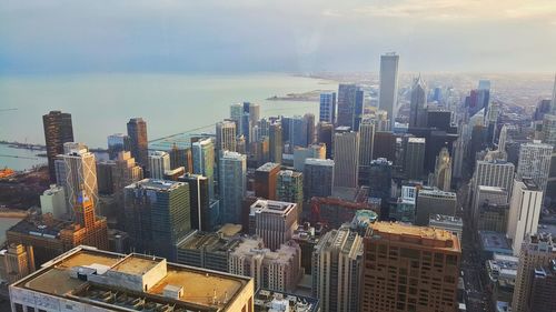 High angle view of cityscape by sea against cloudy sky