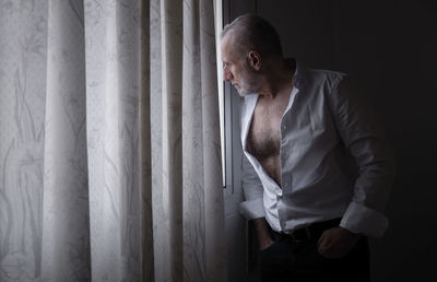 Adult man in white shirt in room looking out window