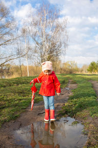 Child plays with umbrella after the rain in red rubber boots and a raincoat.