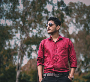 Young man wearing sunglasses standing against trees