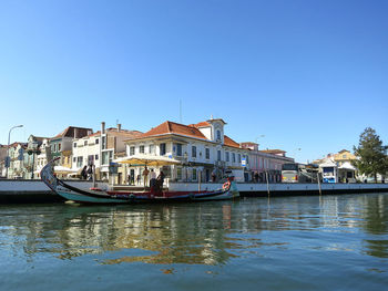 Boats in river by buildings against clear sky