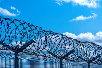 Low angle view of barbed wire fence against blue sky