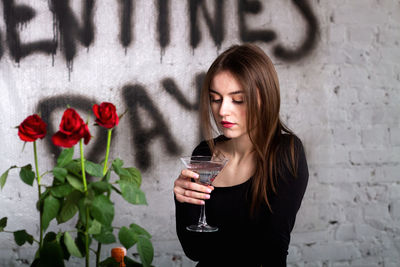 Portrait of young woman drinking water while standing against wall