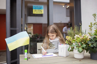 Small girl draws ukrainian flag in safe place abroad in europe where she fled from russian invasion