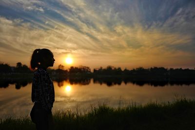 Rear view of silhouette boy on lake against sky during sunset