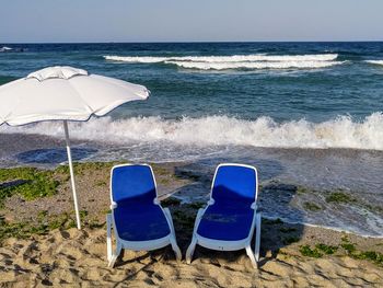 Deck chairs on beach against sky