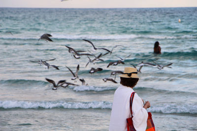 Woman at seashore with flock of birds in background
