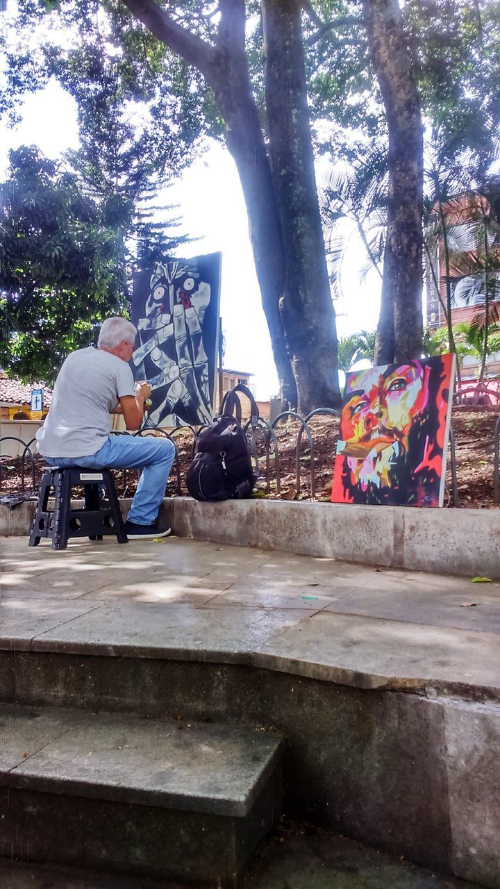 tree, built structure, architecture, building exterior, day, sunlight, lifestyles, table, outdoors, text, leisure activity, men, tree trunk, person, art and craft, railing, bench, art, park - man made space