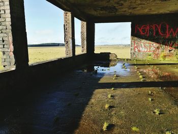 Abandoned building by sea against sky seen through window