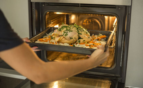 Midsection of woman inserting chicken in oven