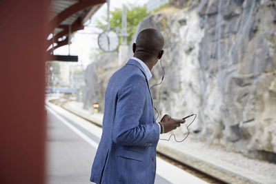 Businessman listening music while waiting at railroad station